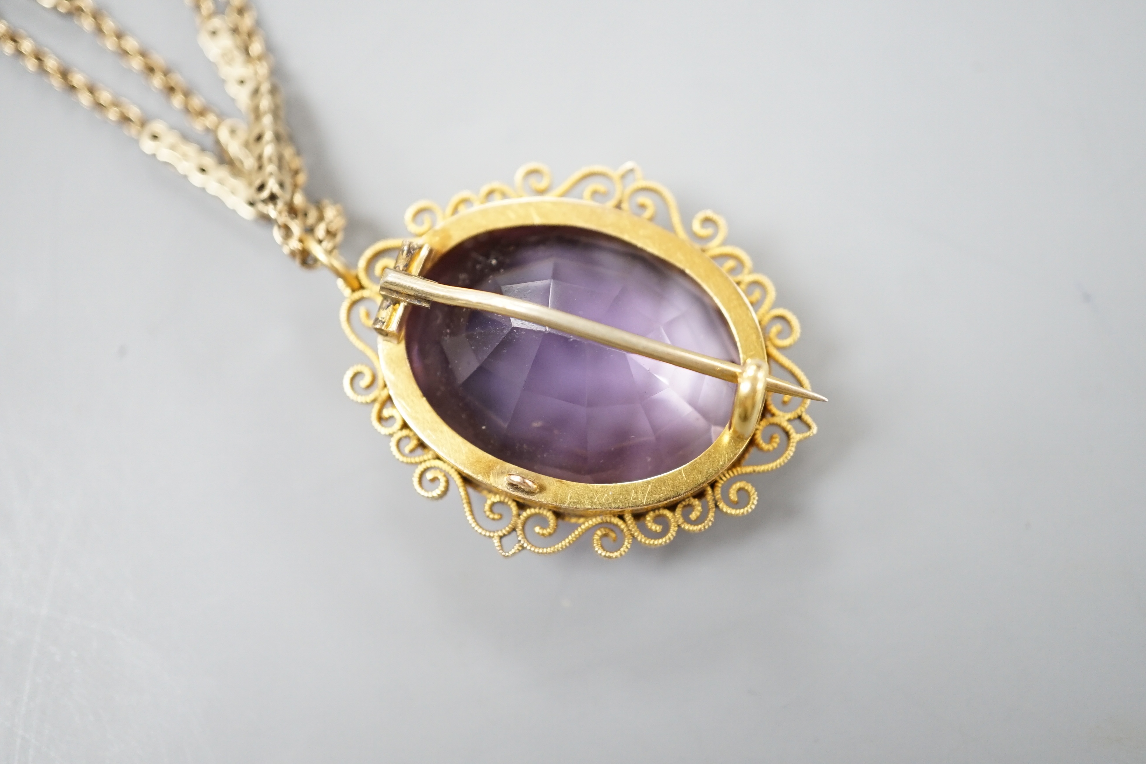 A yellow metal mounted oval cut amethyst pendant brooch, 34mm, gross 13.2 grams, on a Victorian pinchbeck guard chain, 70cm.